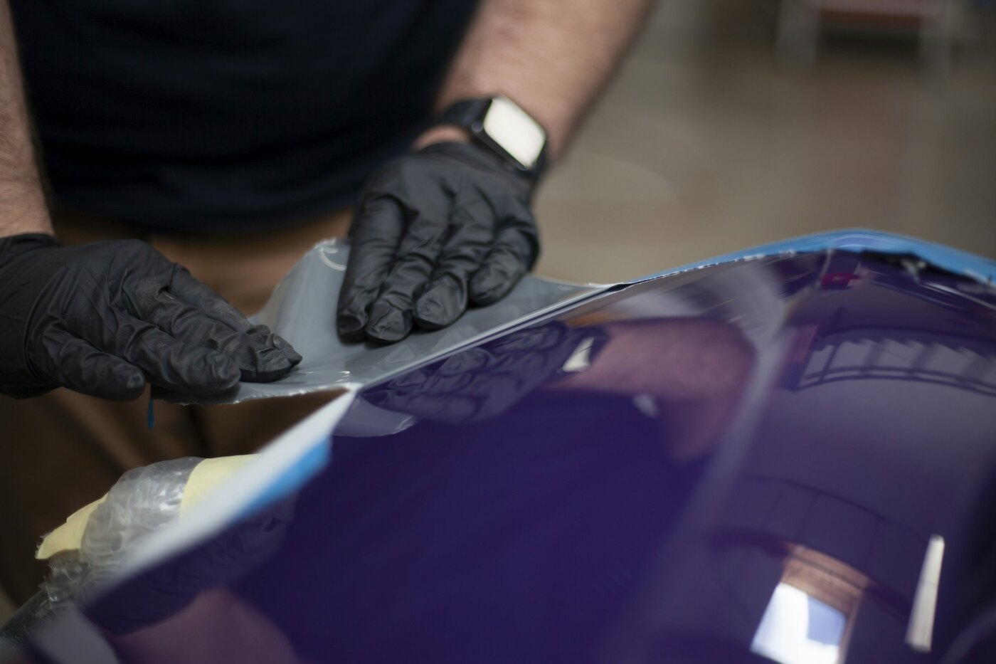 A body-shop technician's gloved hands finishing a glossy, freshly refinished panel